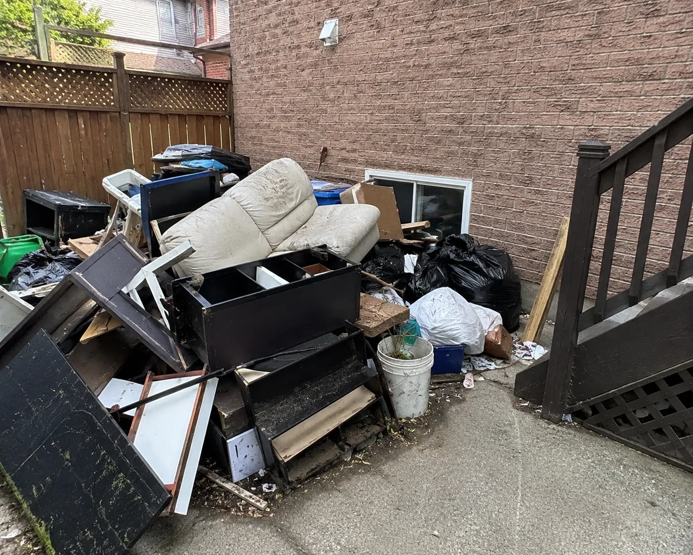 Side yard piled with a sofa, cabinets and garbage bags before junk removal