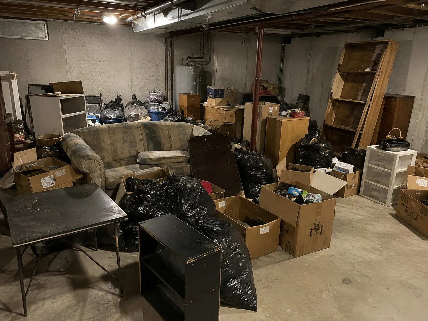 Unfinished basement packed with a couch, boxes and debris before junk removal